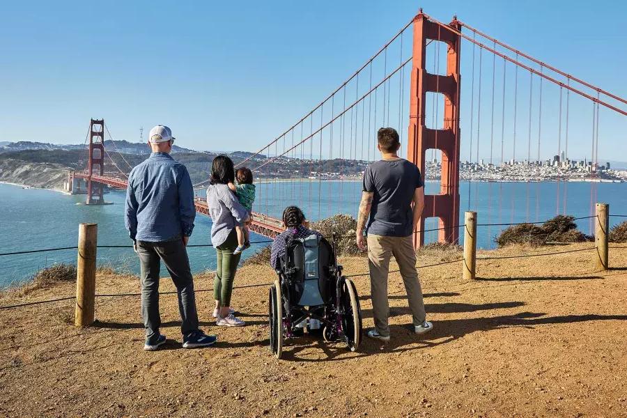 Un grupo de personas, 包括一名轮椅使用者, se ve desde atrás mientras miran el puente Golden Gate desde Marin Headlands.